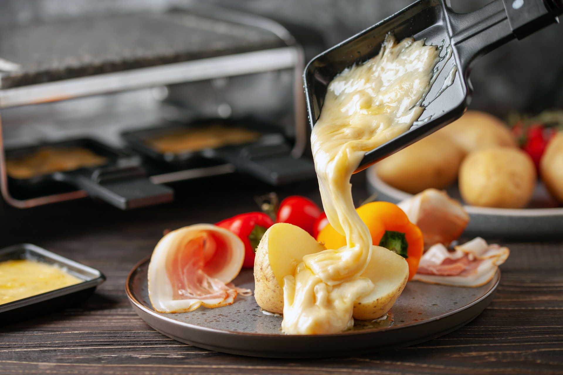 Delicious traditional Swiss melted raclette cheese on diced boiled or baked vegetables served in individual skillets